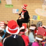 kids listening to a women who is dressed up in a red and white hat