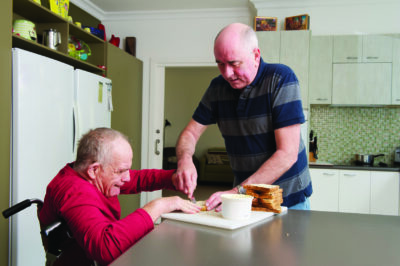 A man helping an older man spread butter on his toast.