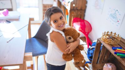 Little girl smiling and holding a teddy bear while in class