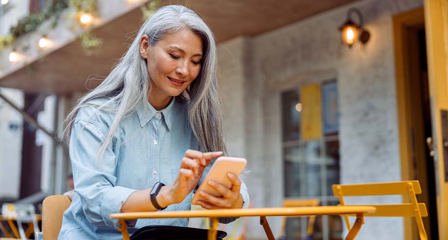 a happy senior women working on mobile phone sitting outside of a restaurant