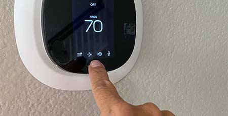 A hand adjusting a digital thermostat